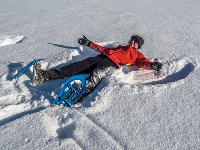 Man in red jacket lying on floor in snow making a snow angel St Zyprian, Italy