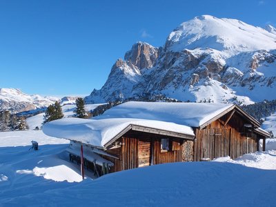 Wooden chalet with snow covered on roof in the Dolomites mountain in winter during sunny day, Italy