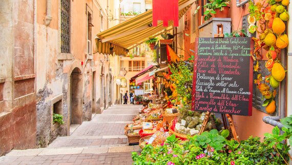 Entrance to local shop in Taormina along street alleyway with plant pots and store goods placed outside stores throughout, Sicily, Italy